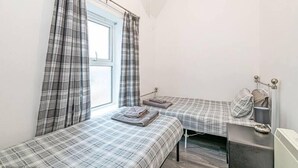 Een kleine, eenvoudige kamer met twee bedden, een raam met gordijnen, een radiator en een nachtkastje.