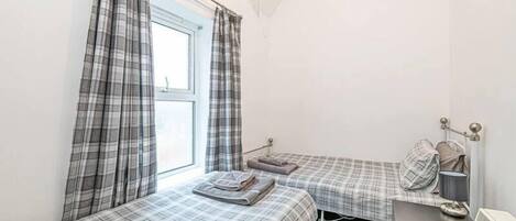 Un alojamiento pequeño y de una sola habitación con dos camas, una ventana con cortinas, un radiador y una mesita de noche.