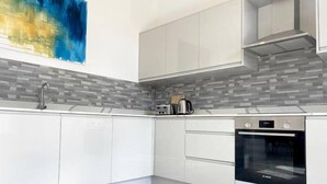 Une cuisine moderne avec des meubles blancs, un four Bosch et un pare-feu en carreaux.