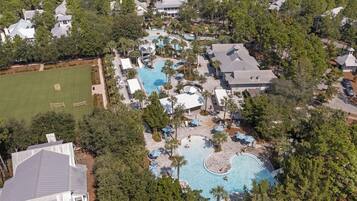 An aerial view of a resort with multiple swimming pools, a large lawn area, and surrounding trees.