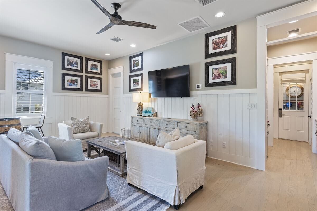 A living room with a ceiling fan, a flat-screen TV mounted on the wall, and a white sofa.
