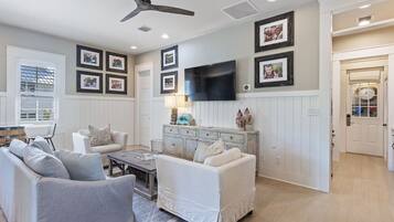 A living room with a ceiling fan, a flat-screen TV mounted on the wall, and a white sofa.