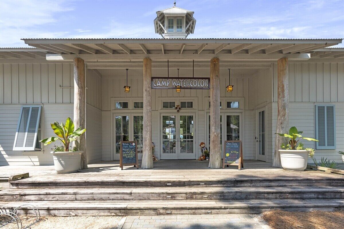 A building with a sign reading 'Camp Watercolor' and a covered entrance with steps leading up to it.