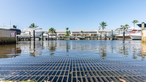 Uma marina com barcos atracados, uma placa indicando 'SLOW NO WAKE ZONE' e um edifício com telhado inclinado.