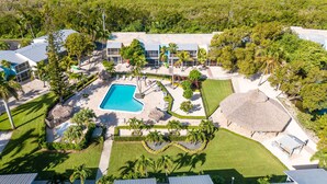 An aerial view of a resort with a central swimming pool, multiple guest rooms, and lush landscaping. - Amazing Key Largo Tropical Paradise 3/3 Townhouse with Water Lagoon view (Key Largo)