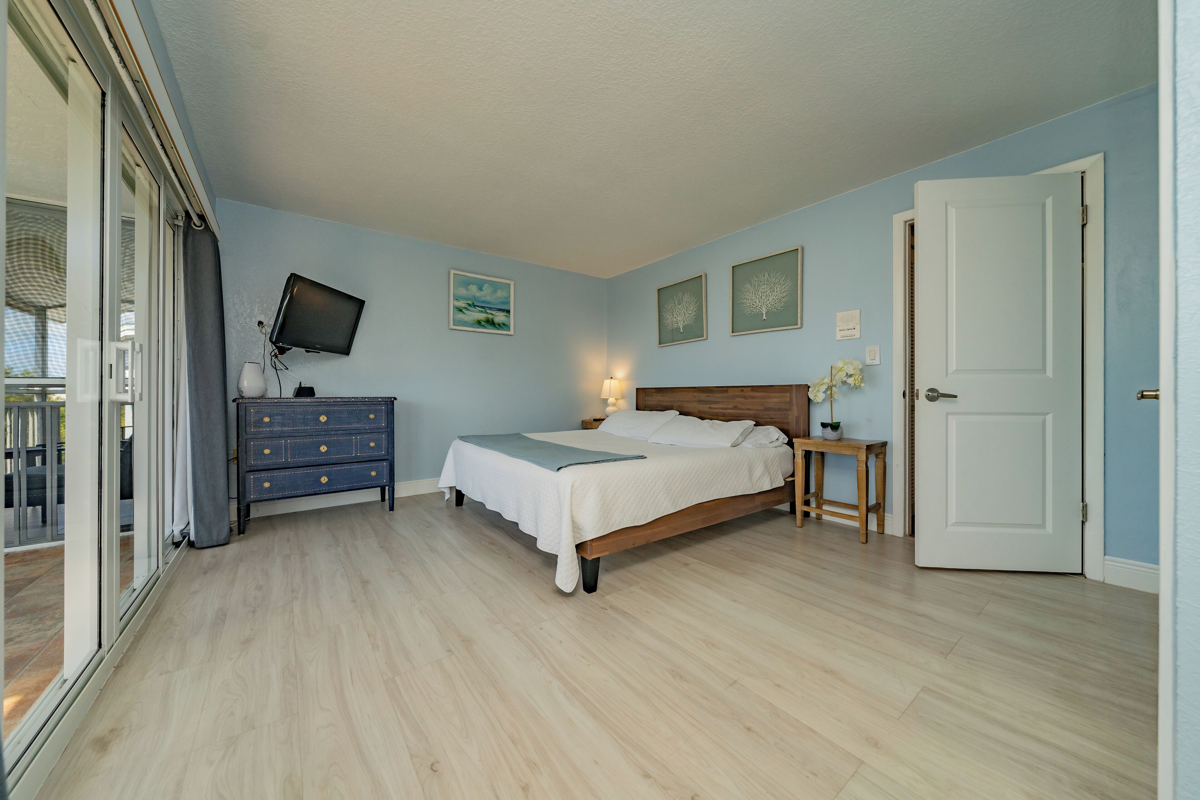 A bedroom with a bed, a dresser, a TV, and a door.