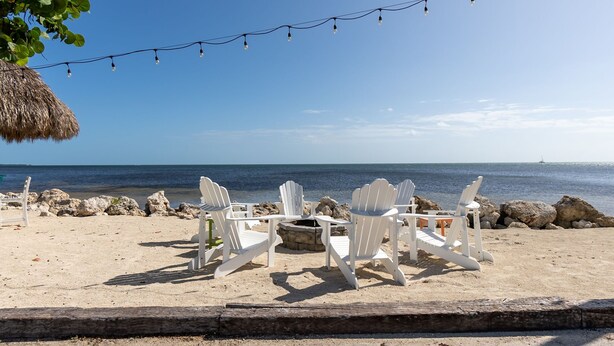 A beach setting with white chairs arranged around a fire pit, overlooking the sea. - Amazing Key Largo Tropical Paradise 3/3 Townhouse with Water Lagoon view (Key Largo)