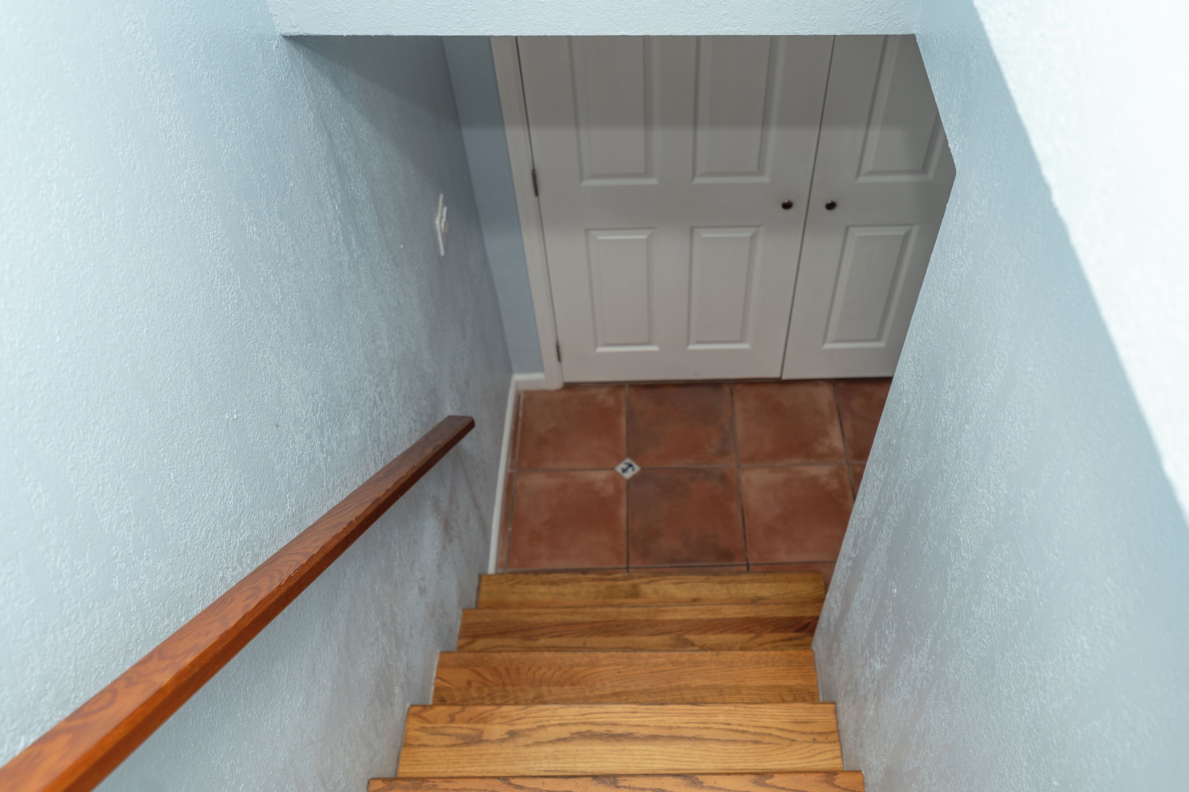 A wooden staircase with a handrail leading to a white door with a keyhole.
