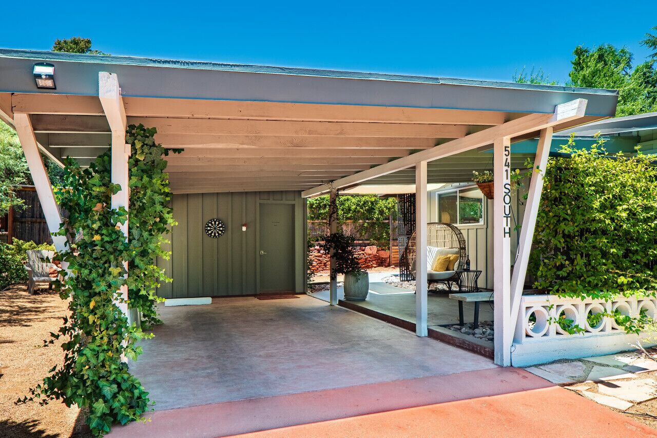 A covered porch with a concrete floor, a green door, and a white railing.