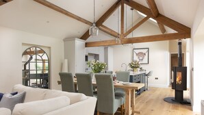 A spacious living area with a high ceiling and exposed wooden beams, a dining table set with chairs, a sofa, and a fireplace.