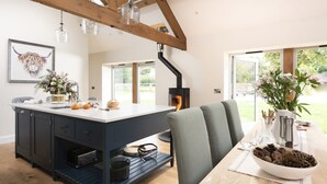 A modern kitchen with a central island, wooden beams, pendant lights, and a view of the outdoors.