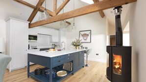 A modern kitchen with a central island, wooden beams, a black stove, and a dining area.