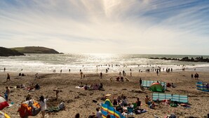 Une plage bondée où l’on voit des gens bronzer et se baigner, ainsi que des tentes et des chaises de plage.