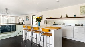Une cuisine moderne dotée d’un îlot central, de tabourets de bar et d’une rambarde en verre donnant sur un balcon.