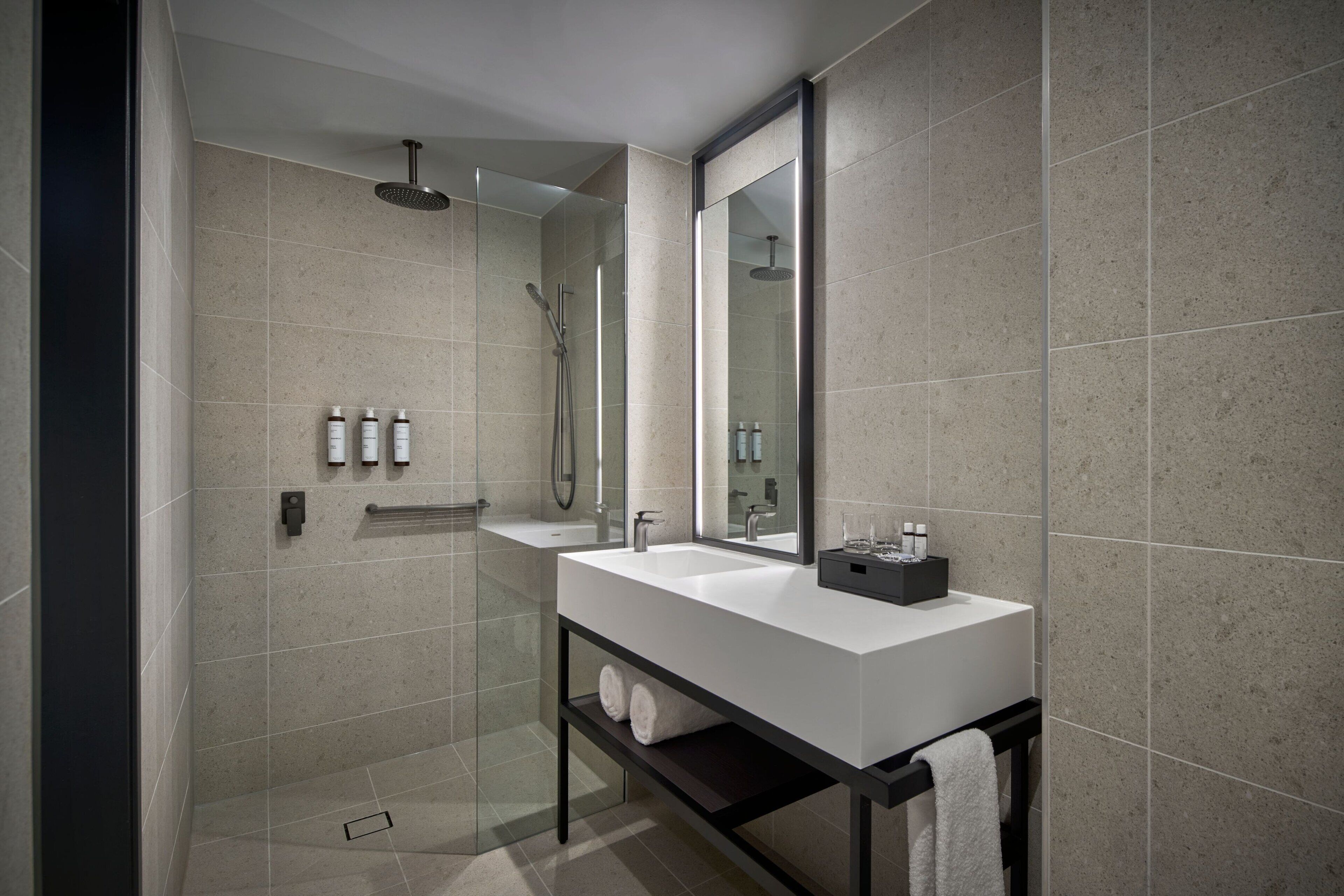 A modern bathroom with a large mirror, a white sink, and a shower area.