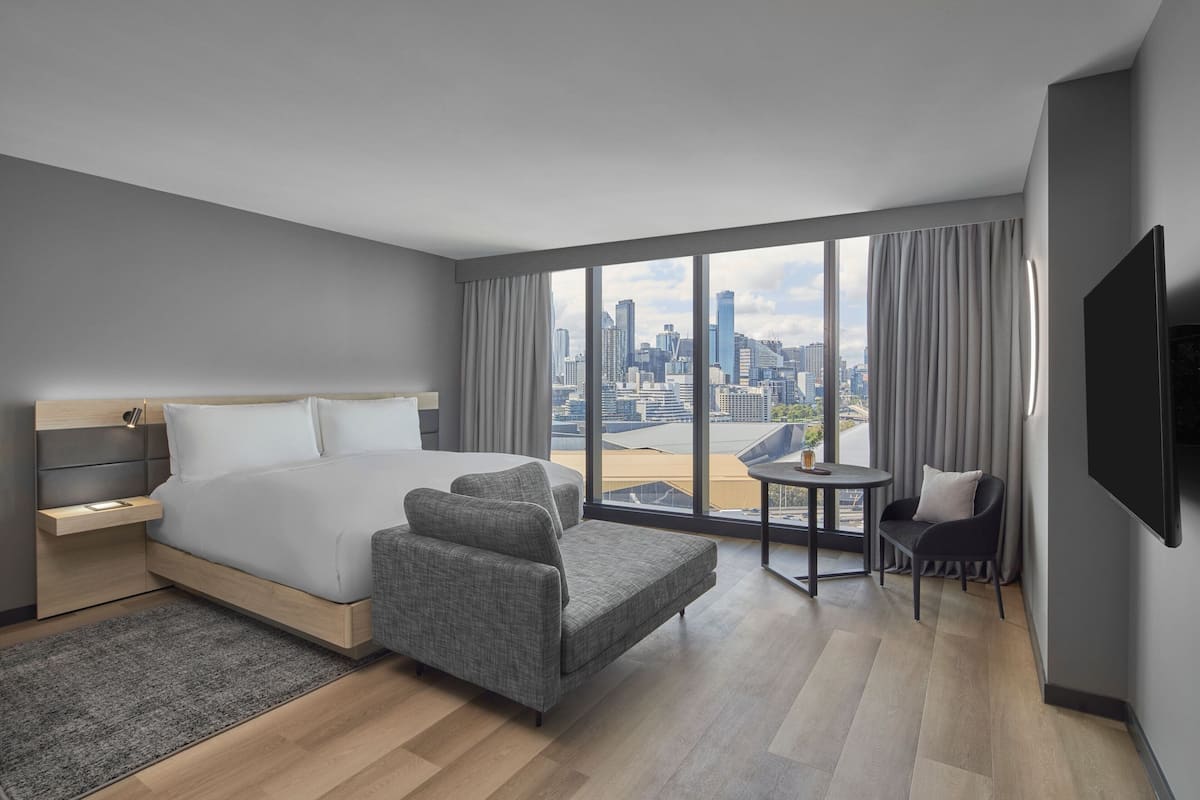 A modern hotel room with a large bed, a seating area, a small table, and a city view.
