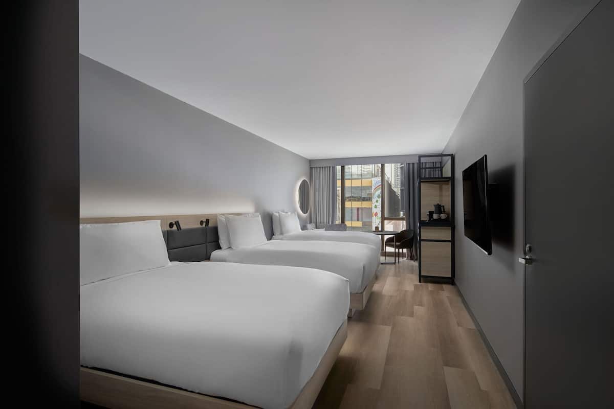 A modern hotel room with two beds, a TV, and a view of the city.