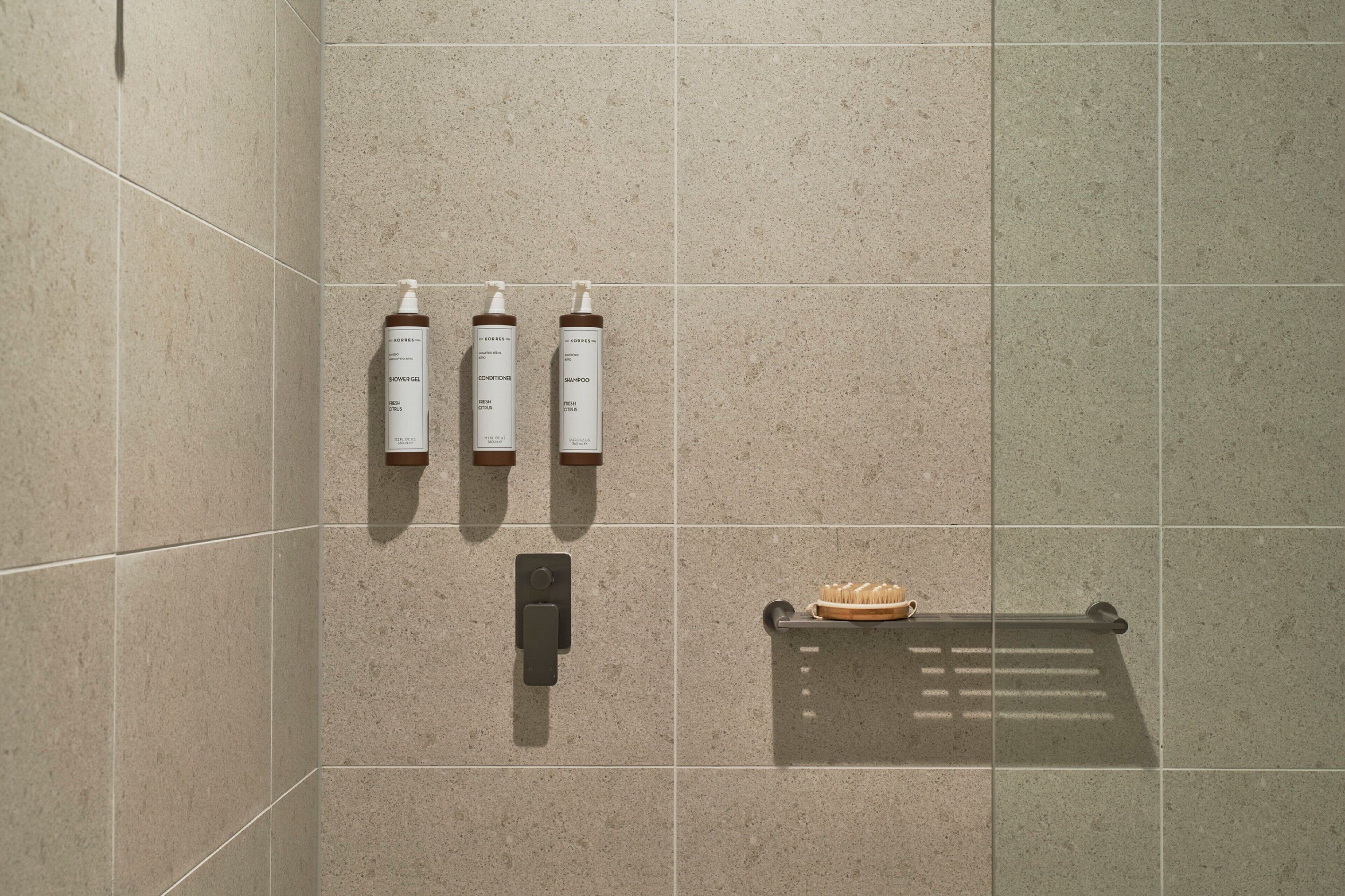 Ein Badezimmer mit drei Pflegeprodukten an der Wand, einem Handtuchhalter mit Handtuch und einer Duscharmatur.