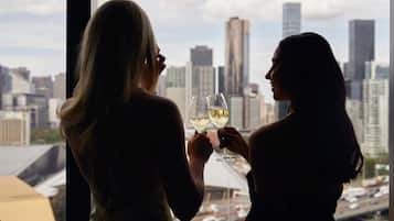 Deux personnes tenant des verres à vin, debout devant une fenêtre et contemplant la vue sur les gratte-ciel de la ville.