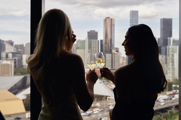 Two people holding wine glasses, facing a city skyline through a window.