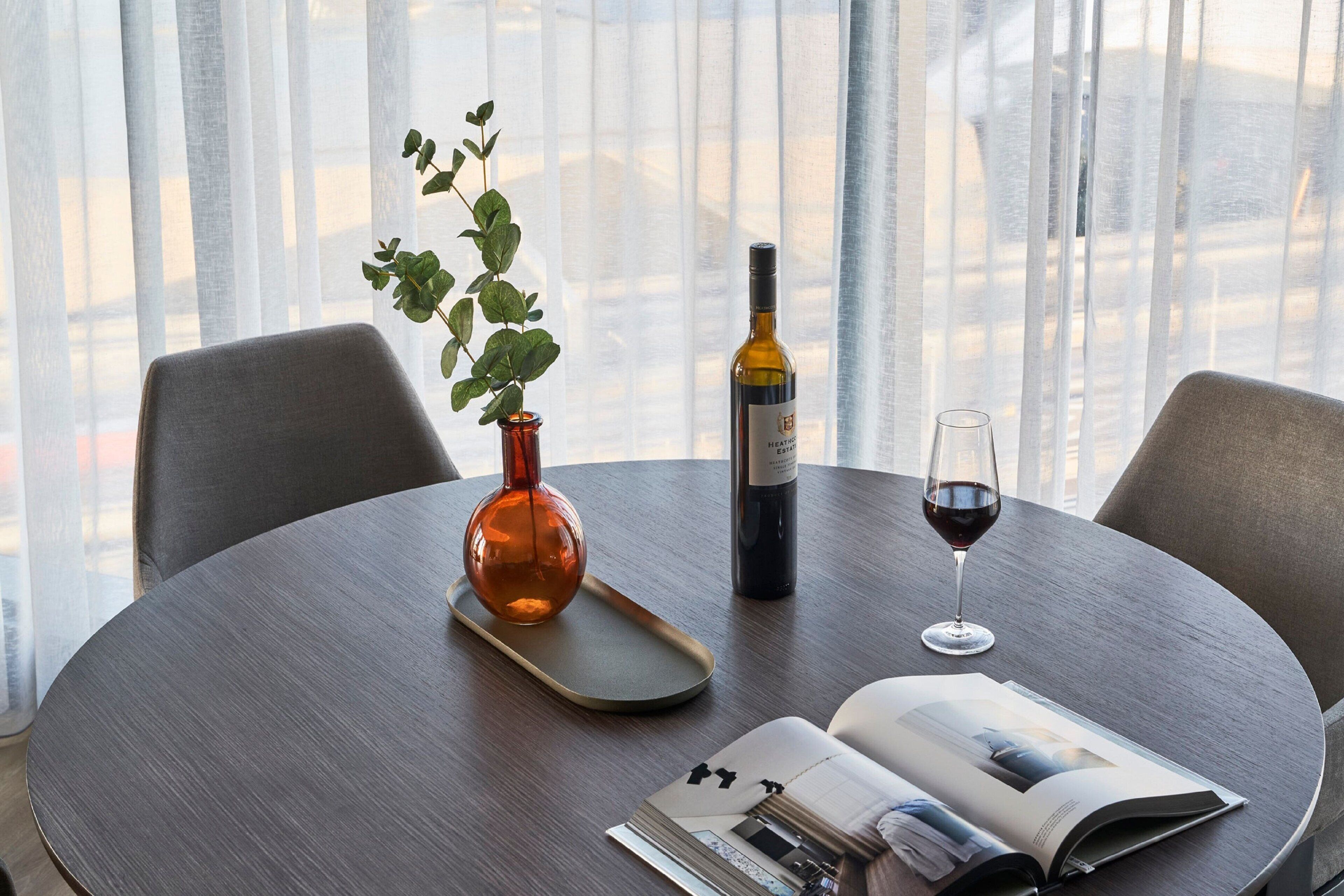 Un tavolo rotondo con una bottiglia di vino, un bicchiere di vino, una rivista e un vaso con una pianta.
