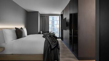 A modern hotel room with a large bed, a flat-screen TV, and a view of the city through the window.