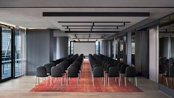 Un salón de conferencias con filas de sillas, ventanas amplias y alfombra roja.