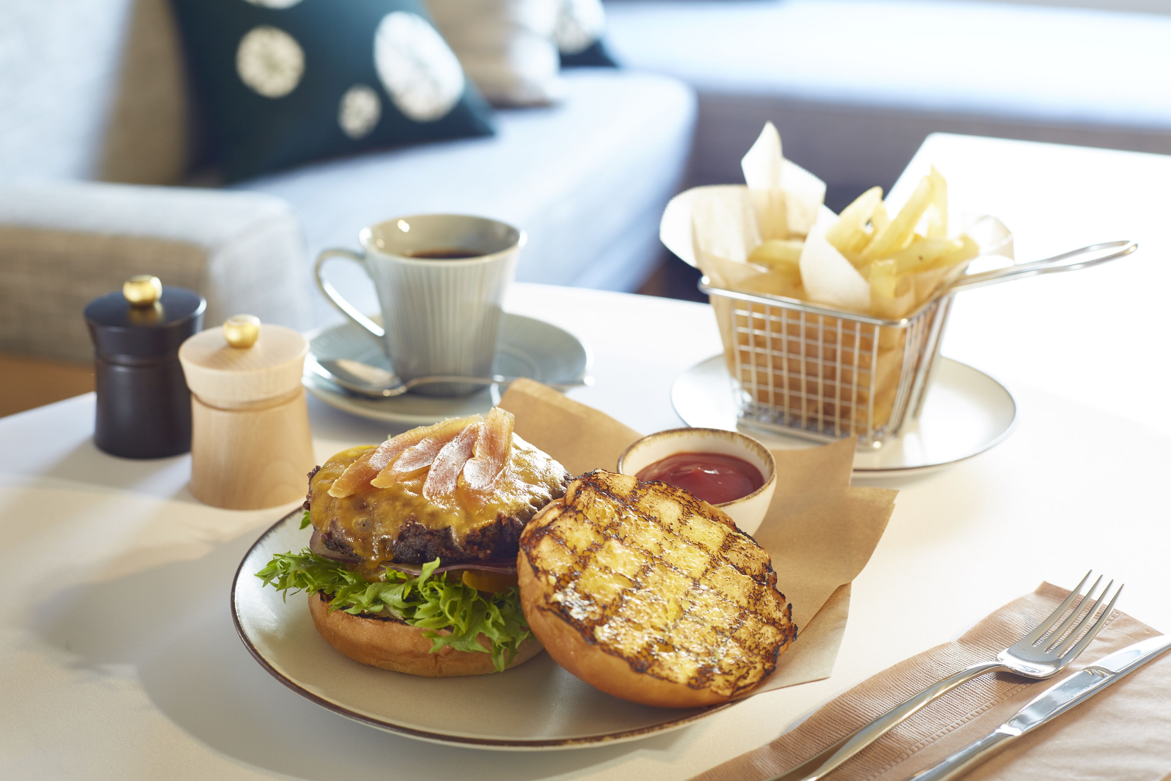 Un plato que incluye una hamburguesa, patata a la parrilla y una taza de café sobre una mesa.