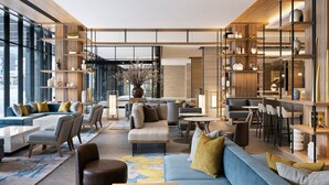 A spacious lobby with a modern design, featuring a mix of seating areas, a coffee bar, and a large bookshelf.