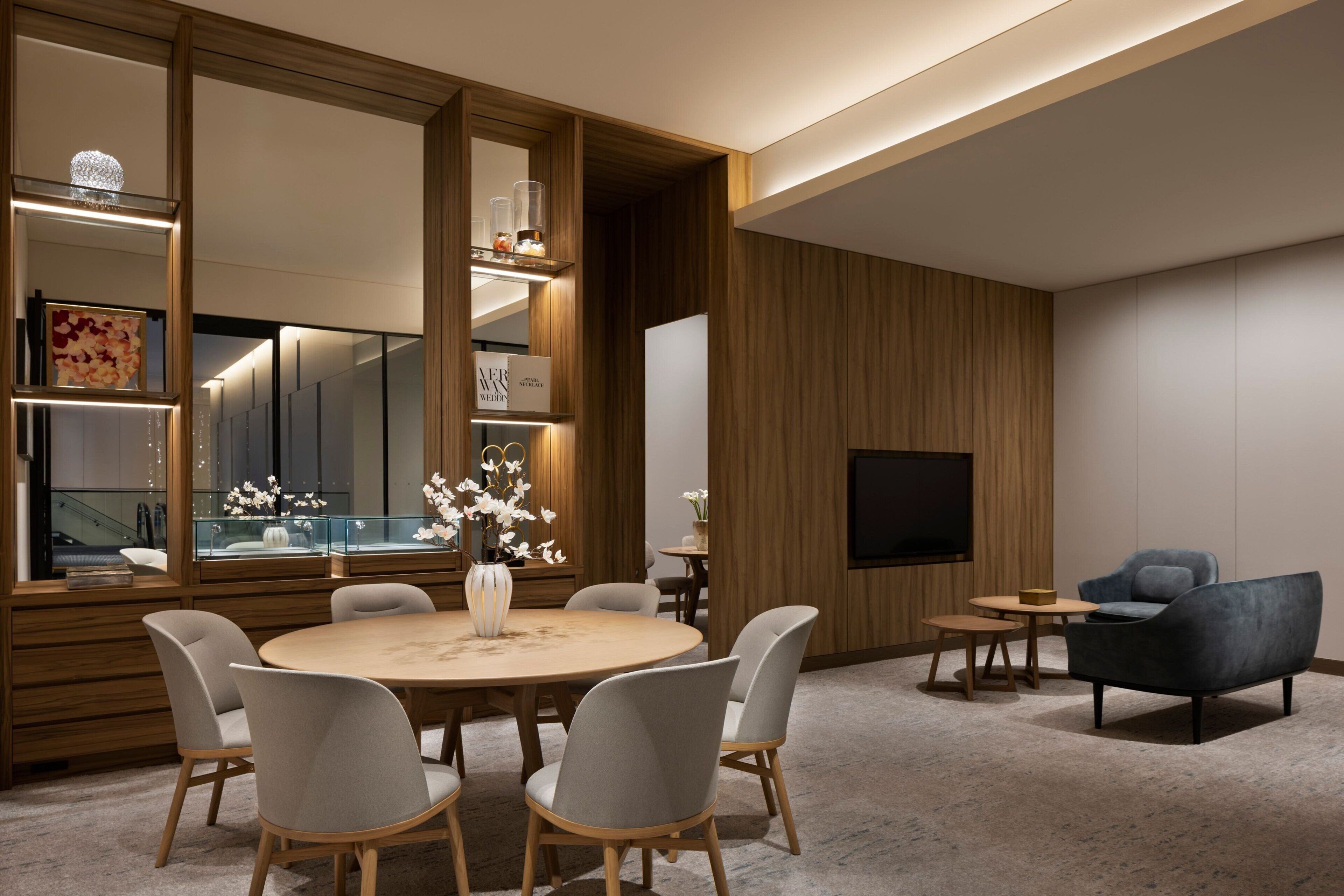A modern living room with a round dining table, grey upholstered chairs, a blue sofa, a TV mounted on the wall, and a wooden accent wall.