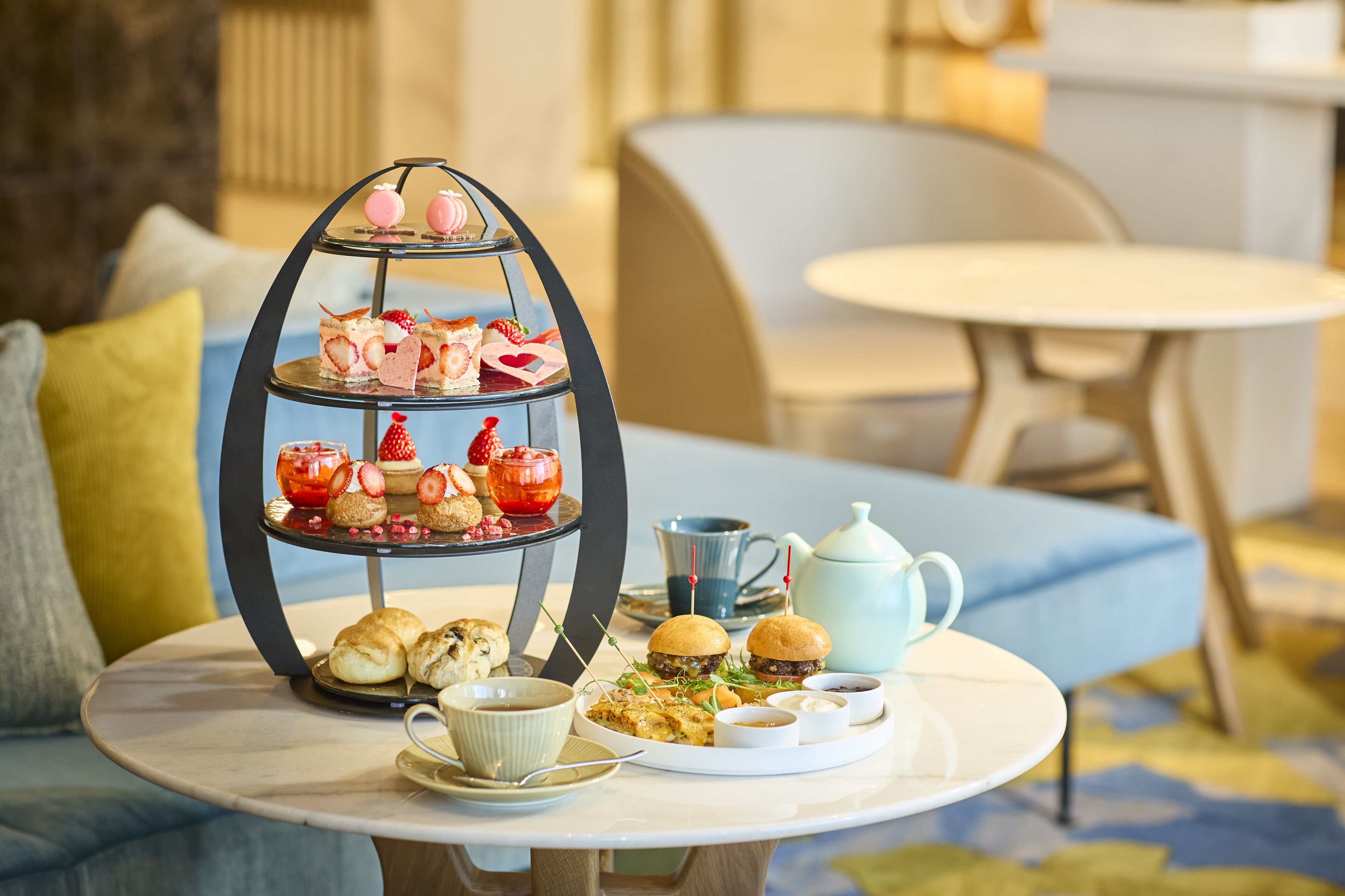 A three-tiered dessert stand with pastries and a teapot on a round table.