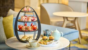 A three-tiered dessert stand with pastries and a teapot on a round table.