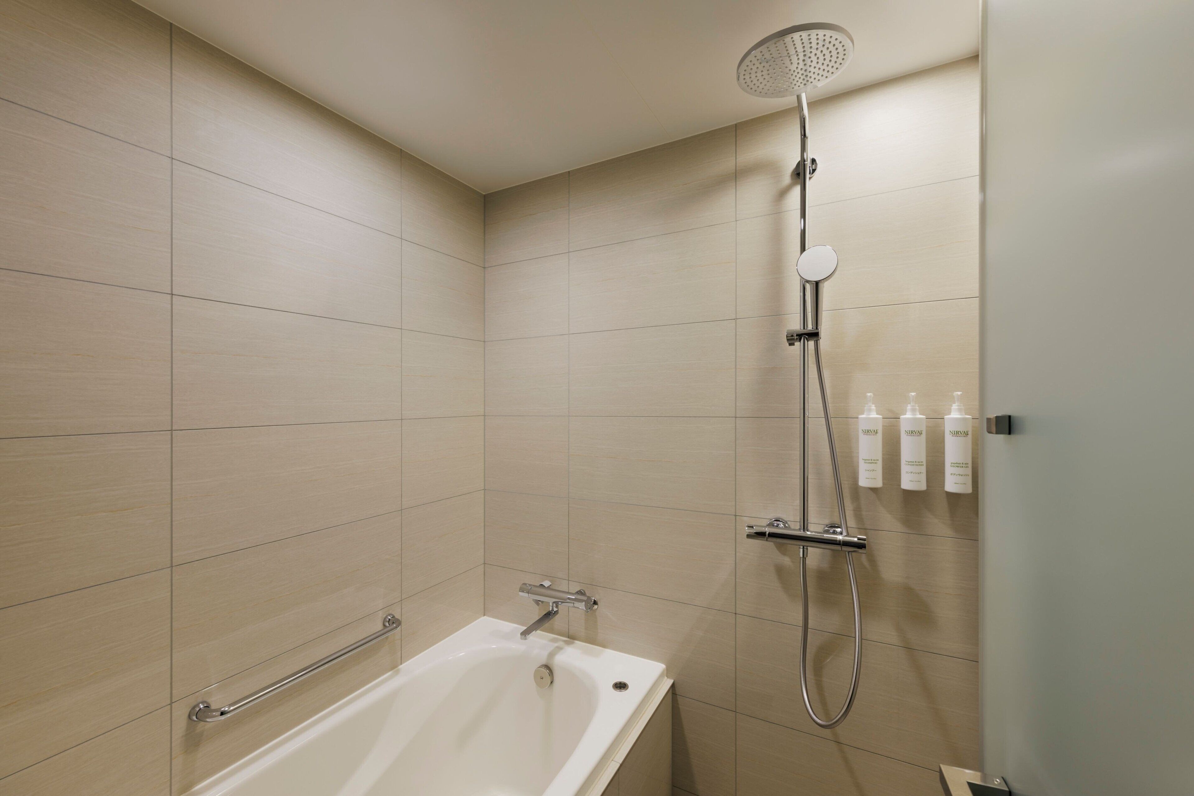 A modern bathroom with a bathtub, a showerhead, and toiletries on the wall.