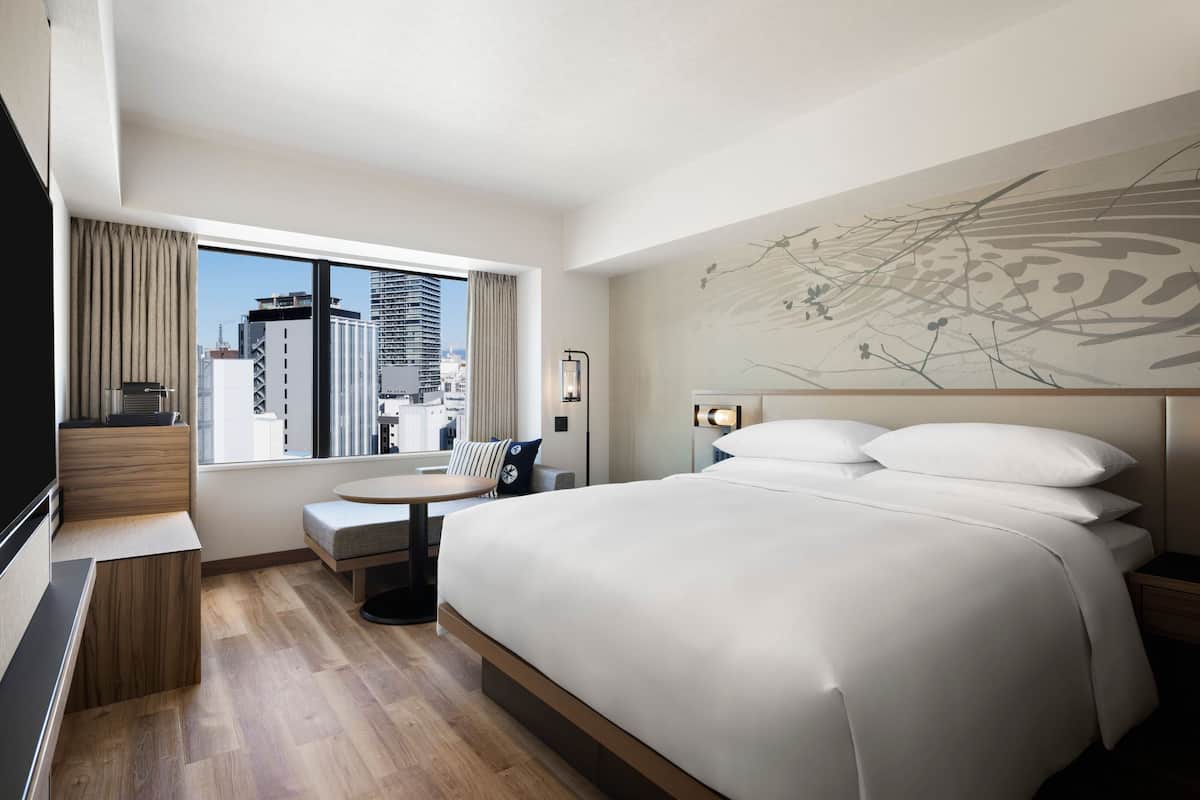 A modern hotel room with a large bed, a desk, and a view of the city skyline.