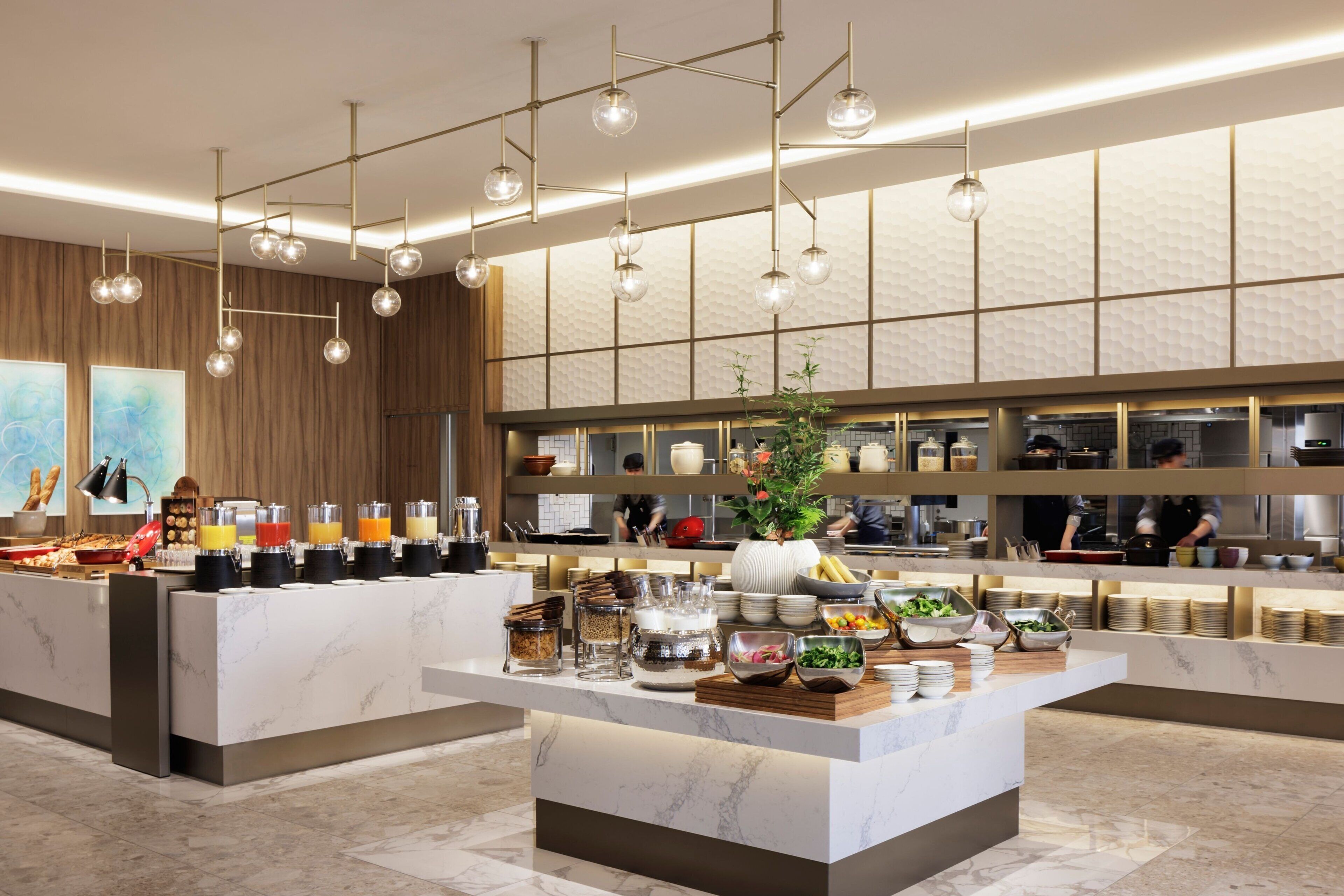 A modern breakfast bar with marble countertops, a variety of food and drink options, and hanging pendant lights.