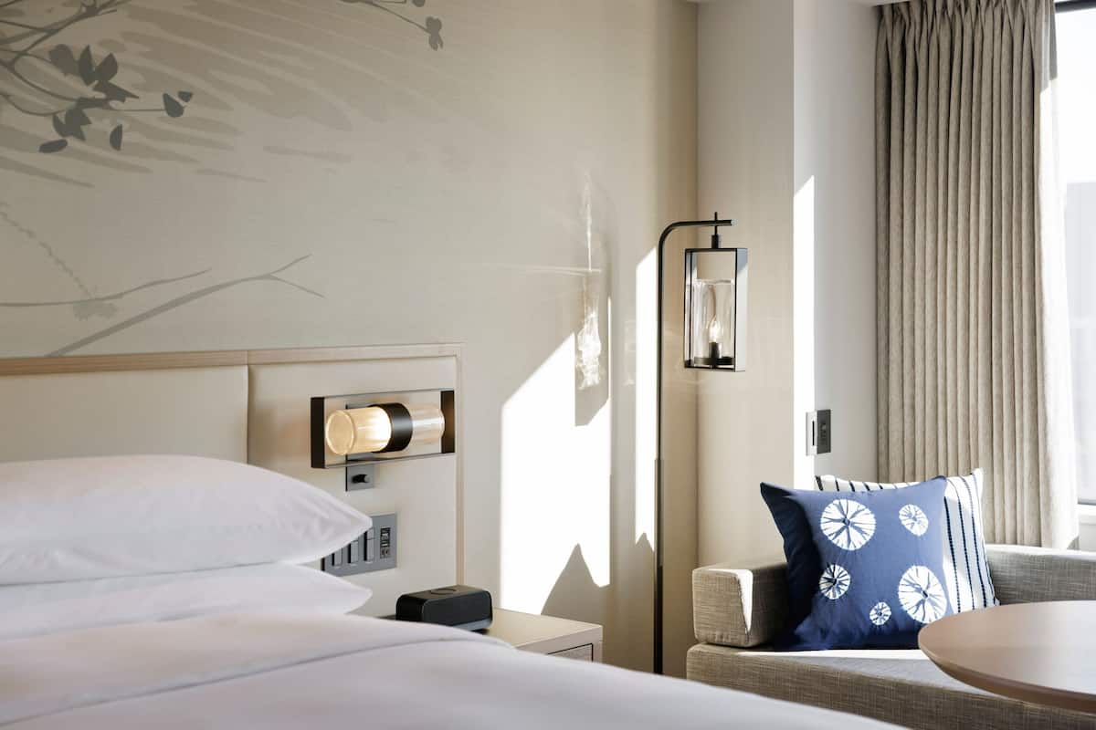 A hotel room with a bed, a bedside table with a lamp, a sofa, and a round table.