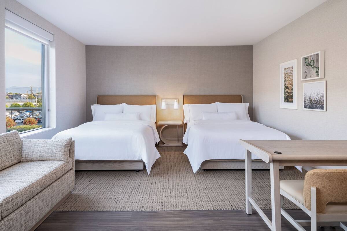 A hotel room with two beds, a sofa, a table, and a view of the city.