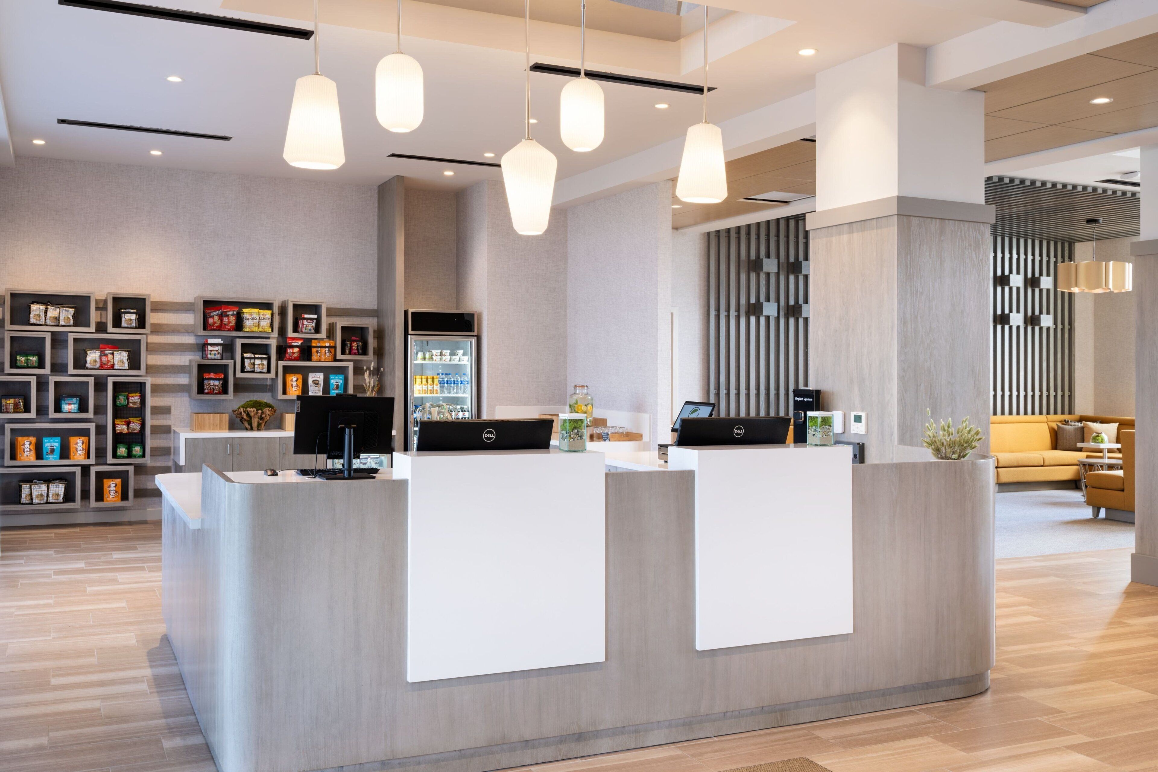Un área de recepción moderna con un mostrador central, diversas opciones de asientos y una exhibición de productos en estanterías.