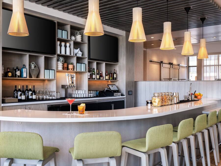 Zona de bar moderna amb un taulell allargat, diverses làmpades penjants i tamborets de bar.