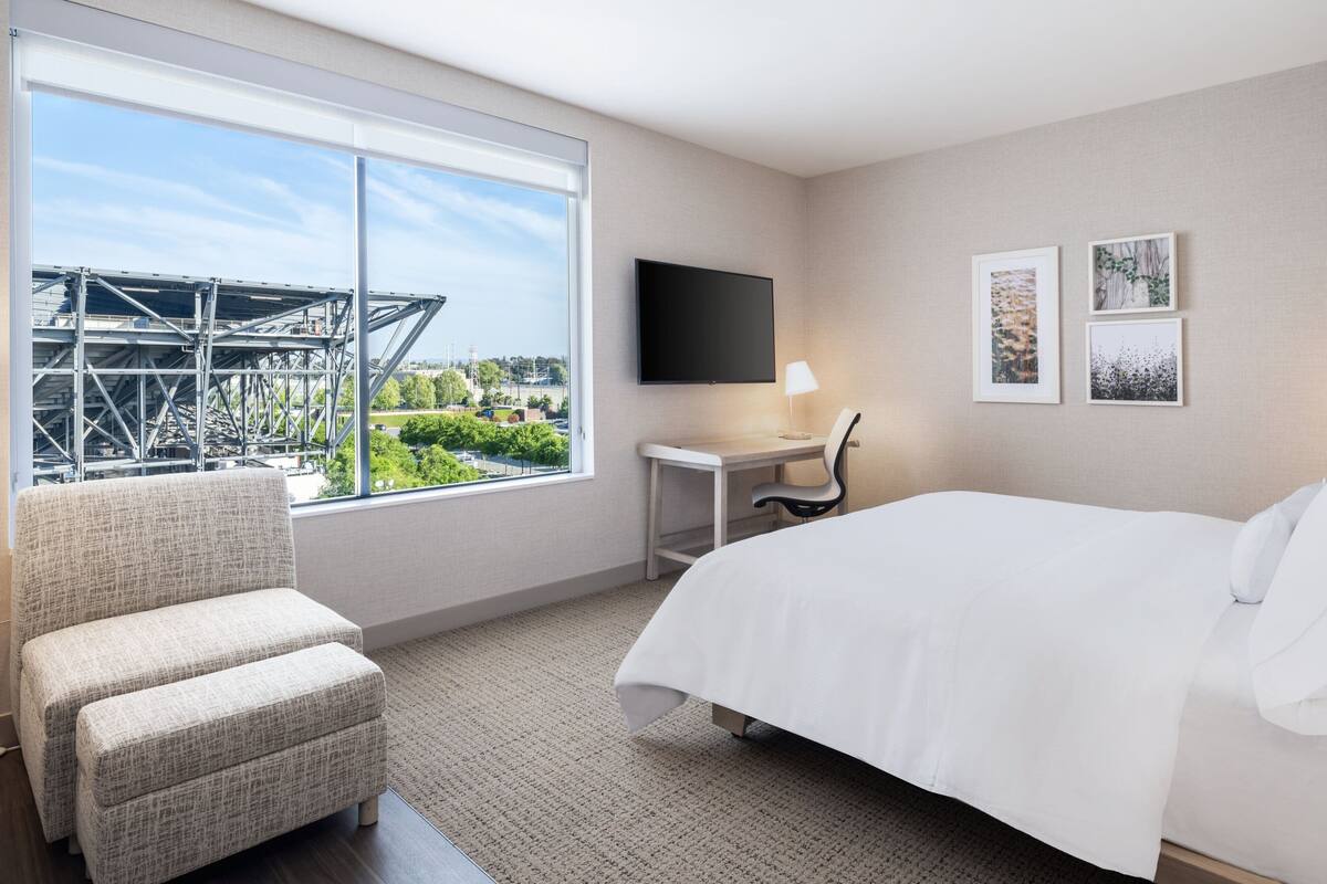A hotel room with a large window, a bed, a desk, and a chair.