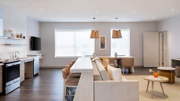 Una cocina moderna con zona de comedor, un sofá y una mesita con un libro y una naranja.