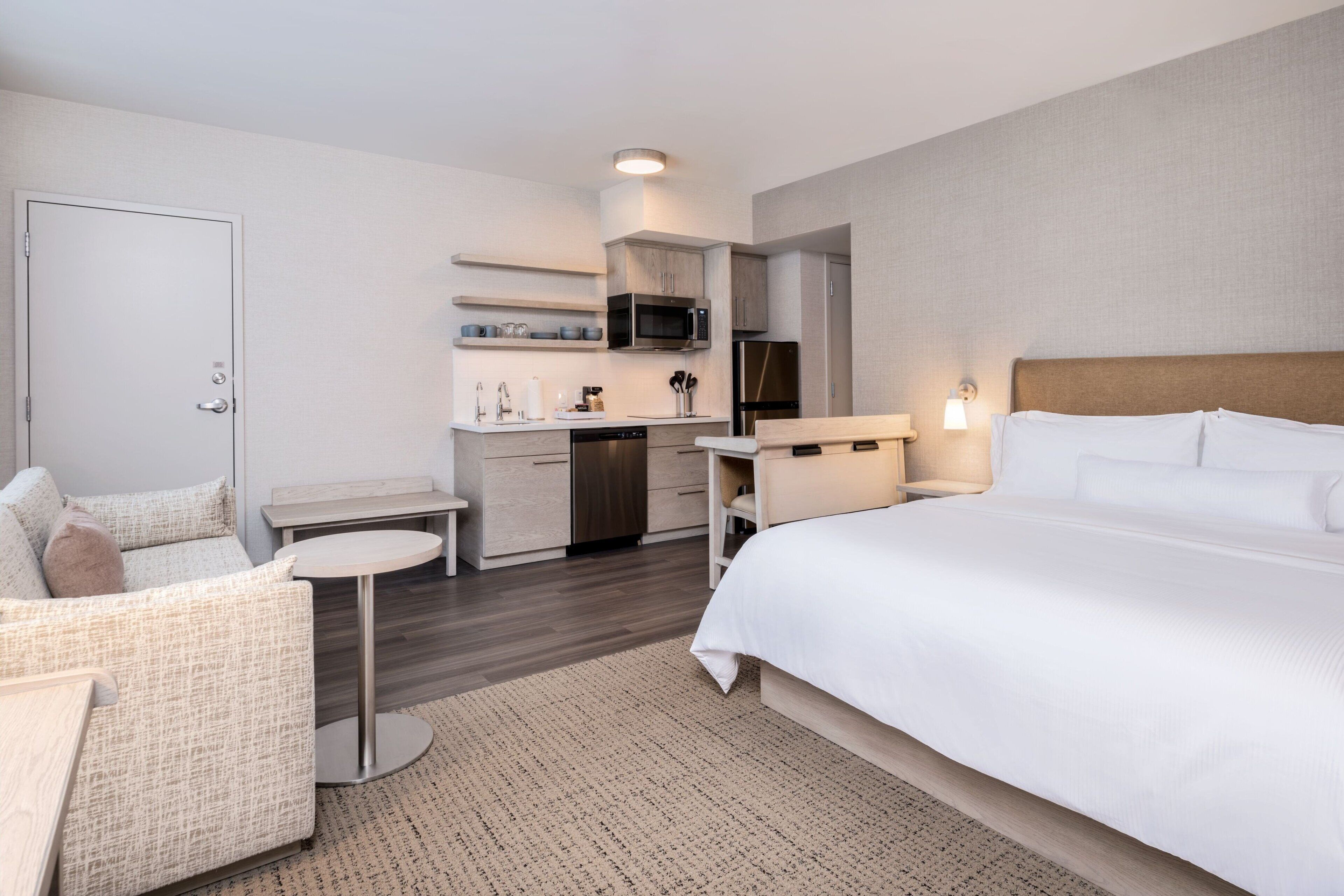 A hotel room with a bed, a small desk, a kitchenette, and a sofa.