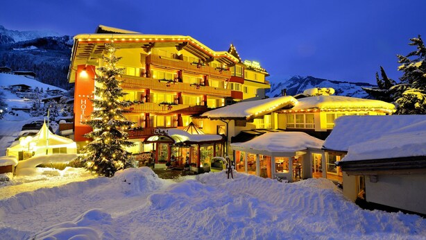 A multi-story hotel with balconies, surrounded by snow-covered mountains and a lit-up facade. - Votters Hotel (Kaprun)