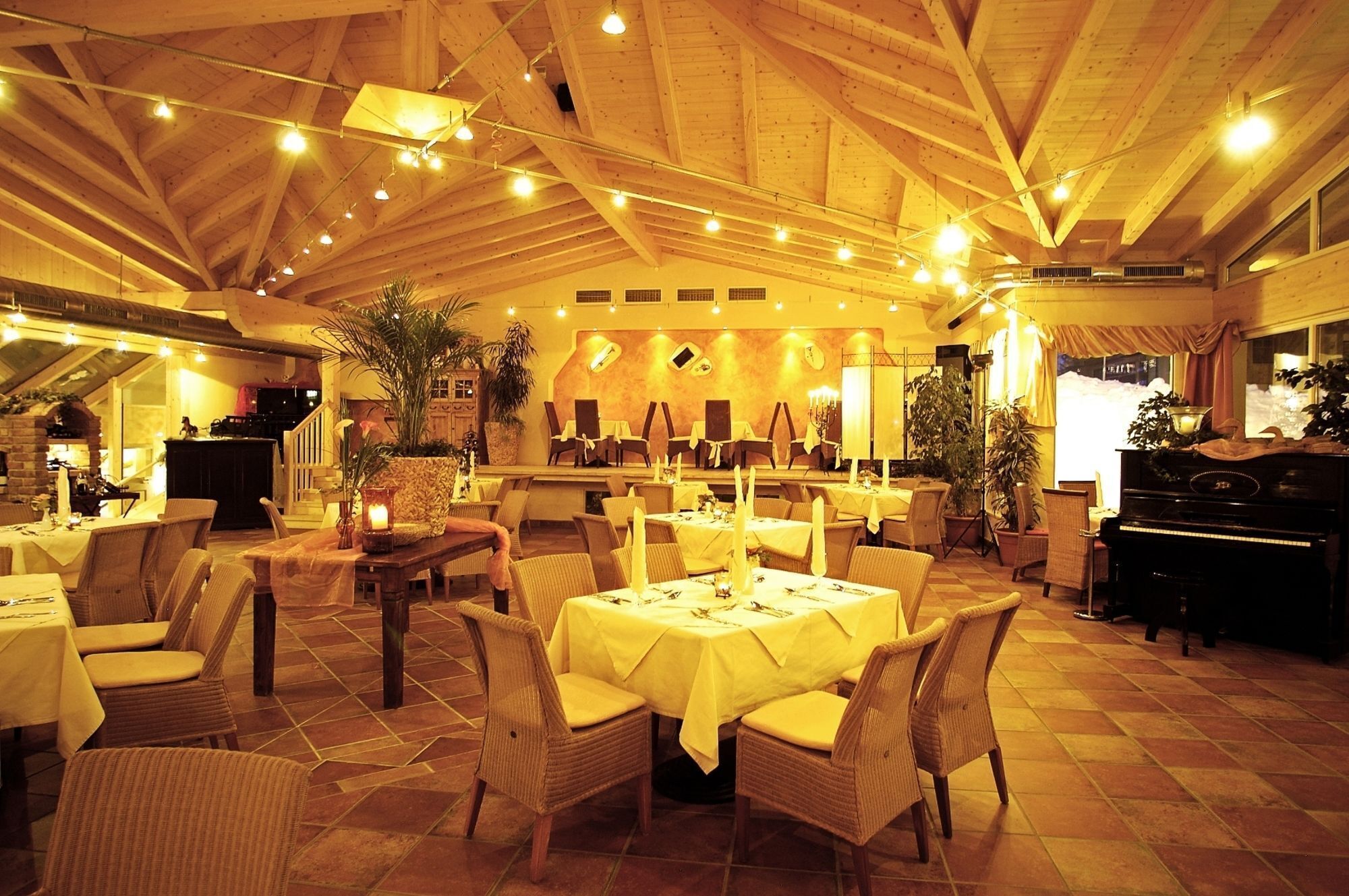 A spacious dining area with high ceilings and wooden beams, featuring multiple tables set for dining, surrounded by wicker chairs.