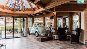 A wooden interior with a vintage car display, large windows, and a chandelier. - Votters Hotel (Kaprun)