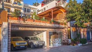 A hotel with a covered parking area, two cars parked inside, and a balcony with plants. - Ferah Hotel (Kaş)