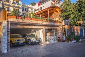 A hotel with a covered parking area, two cars parked inside, and a balcony with plants. - Ferah Hotel (Kaş)