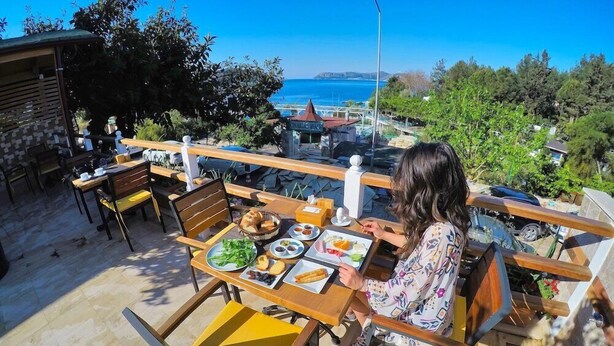 A dining area with a table set for two, overlooking a scenic view of the sea and hills. - Ferah Hotel (Kaş)