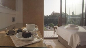 A hotel room with a balcony, a bed with a white blanket, a table with a plate of food and a cup, and a pair of sunglasses on the table. - Ferah Hotel (Kaş)