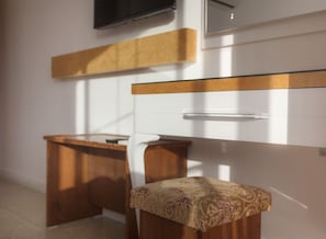 A small, modern room with a wooden desk and a chair, a white wall with a wooden panel, and a mirror above the desk. - Ferah Hotel (Kaş)